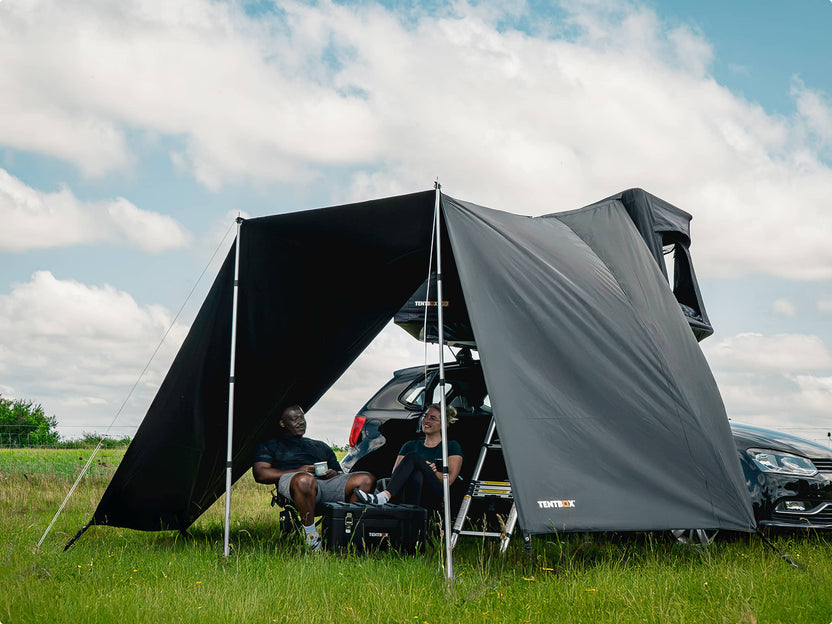 Two people sitting under the TentBox GO Tunnel Awning in a grassy field.